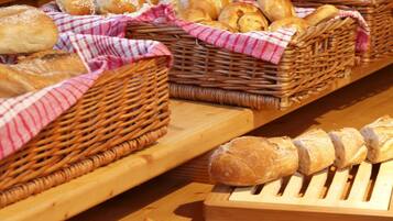 Uma mesa de buffet com diversos pães e doces dispostos em cestos de vime e bandejas de madeira.