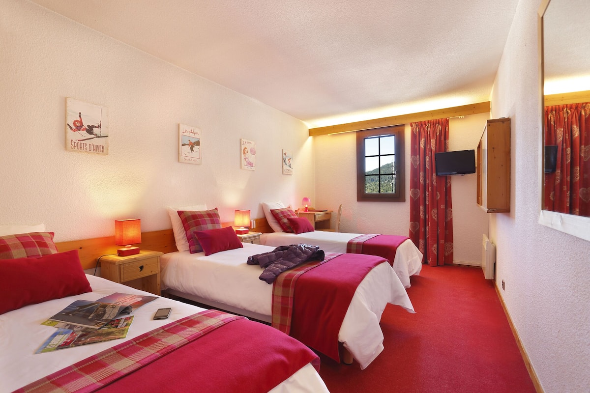 A hotel room with three beds, a TV, a window with curtains, and wall art.