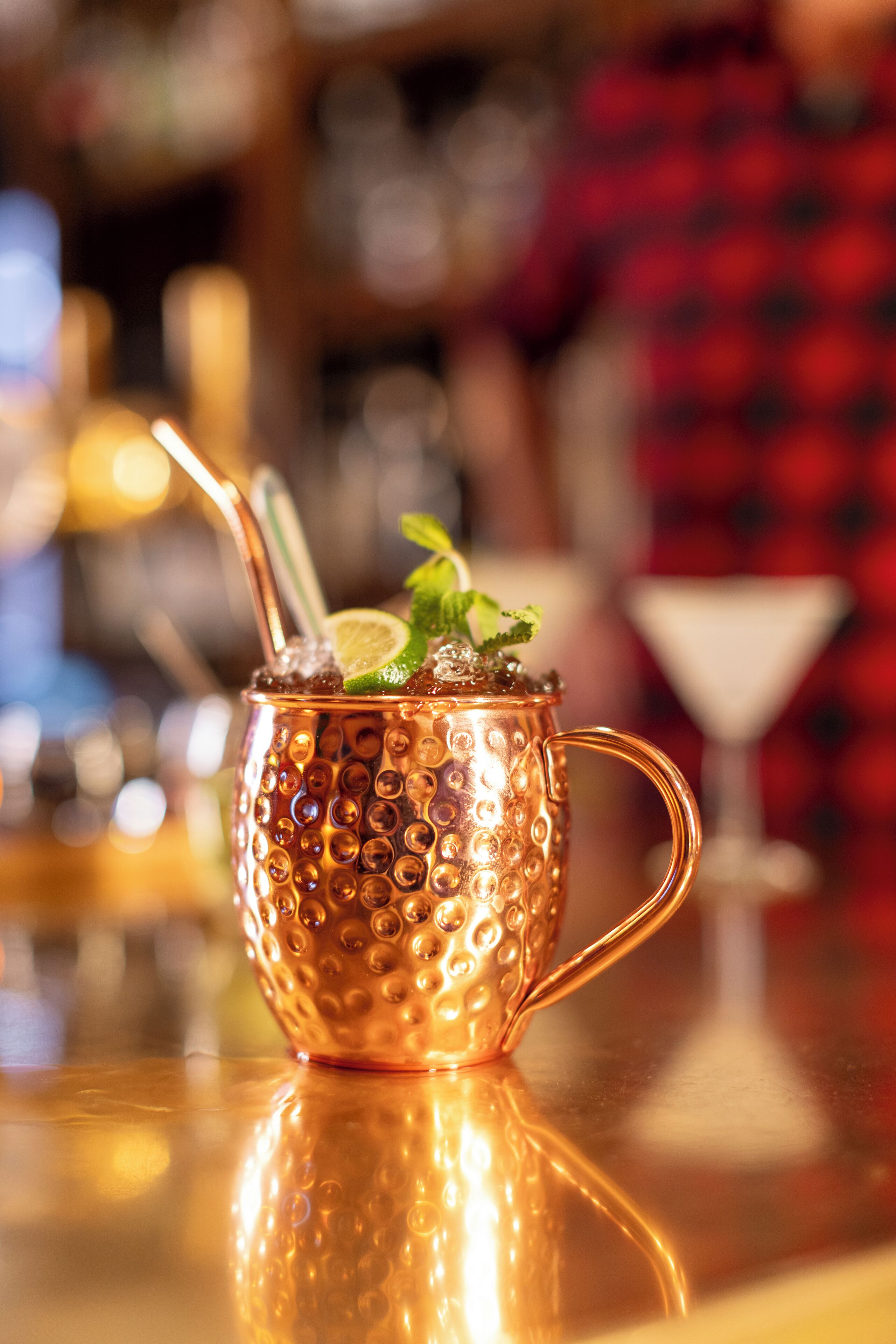 A copper mug with a handle, containing a lime wedge and mint leaves, with a straw.