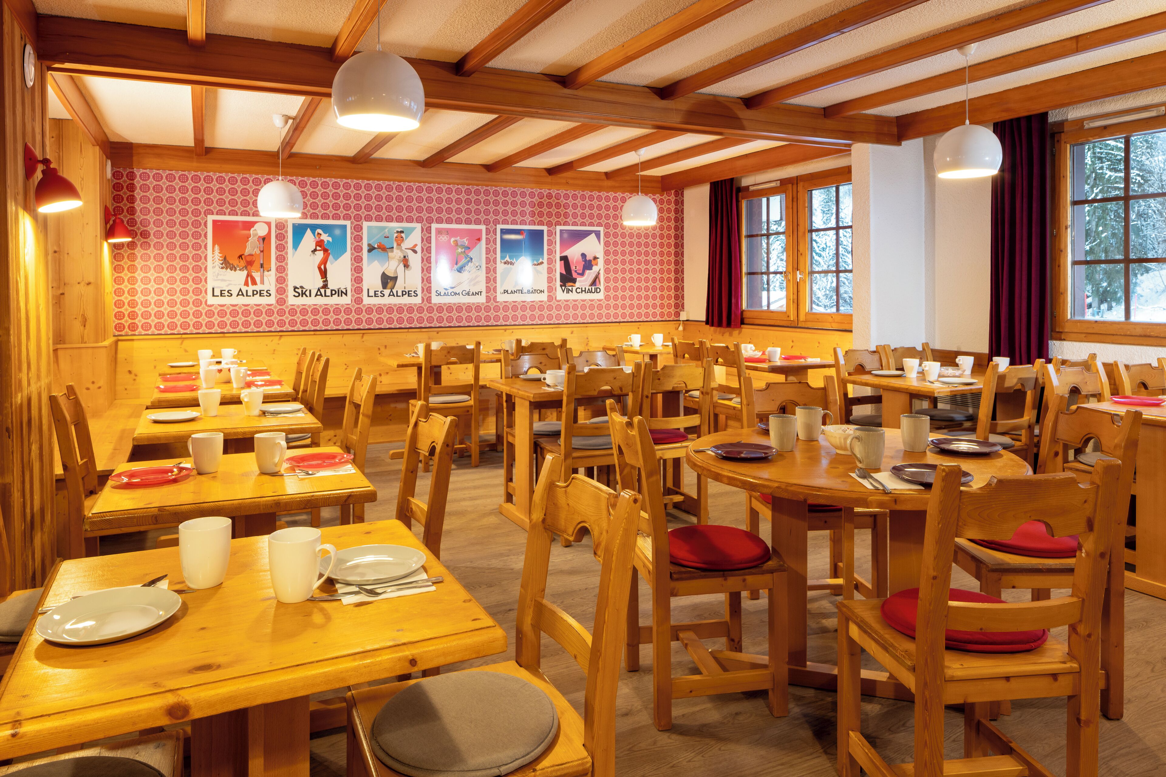 A dining area with wooden tables and chairs, posters on the wall, and large windows.
