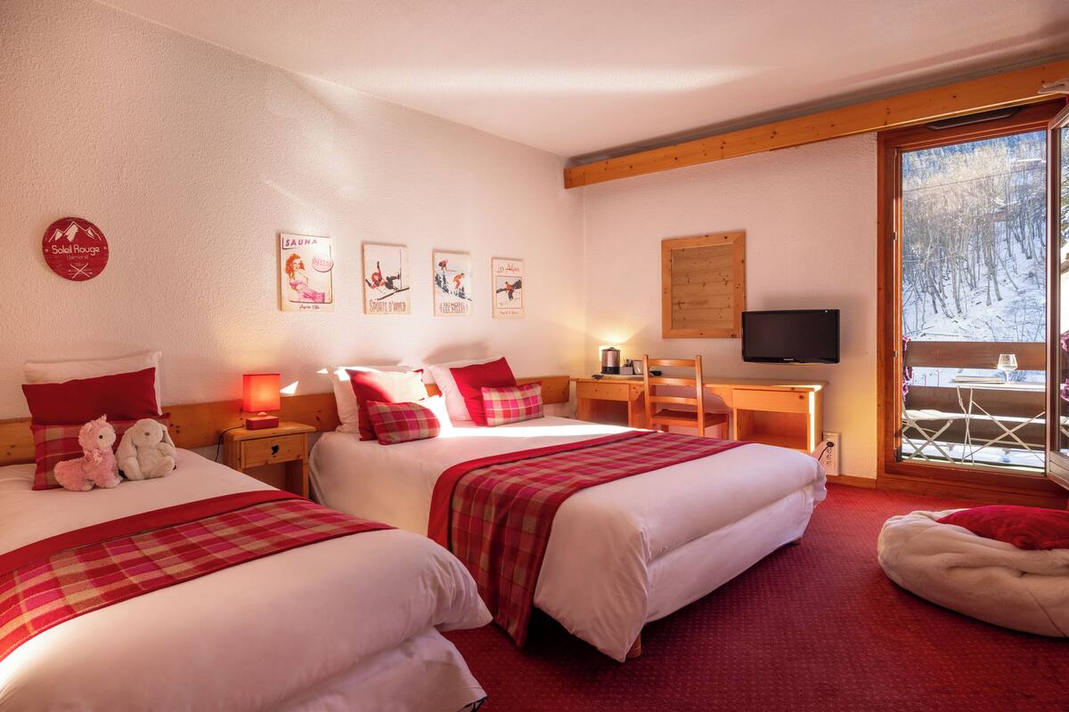 A hotel room with two beds, a desk, a chair, and a TV.
