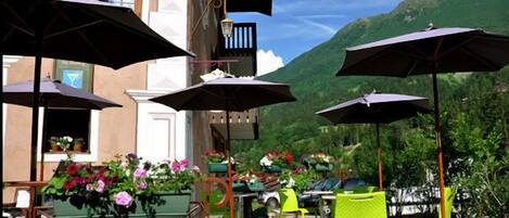 An outdoor patio with green and yellow chairs, black umbrellas, and potted plants.