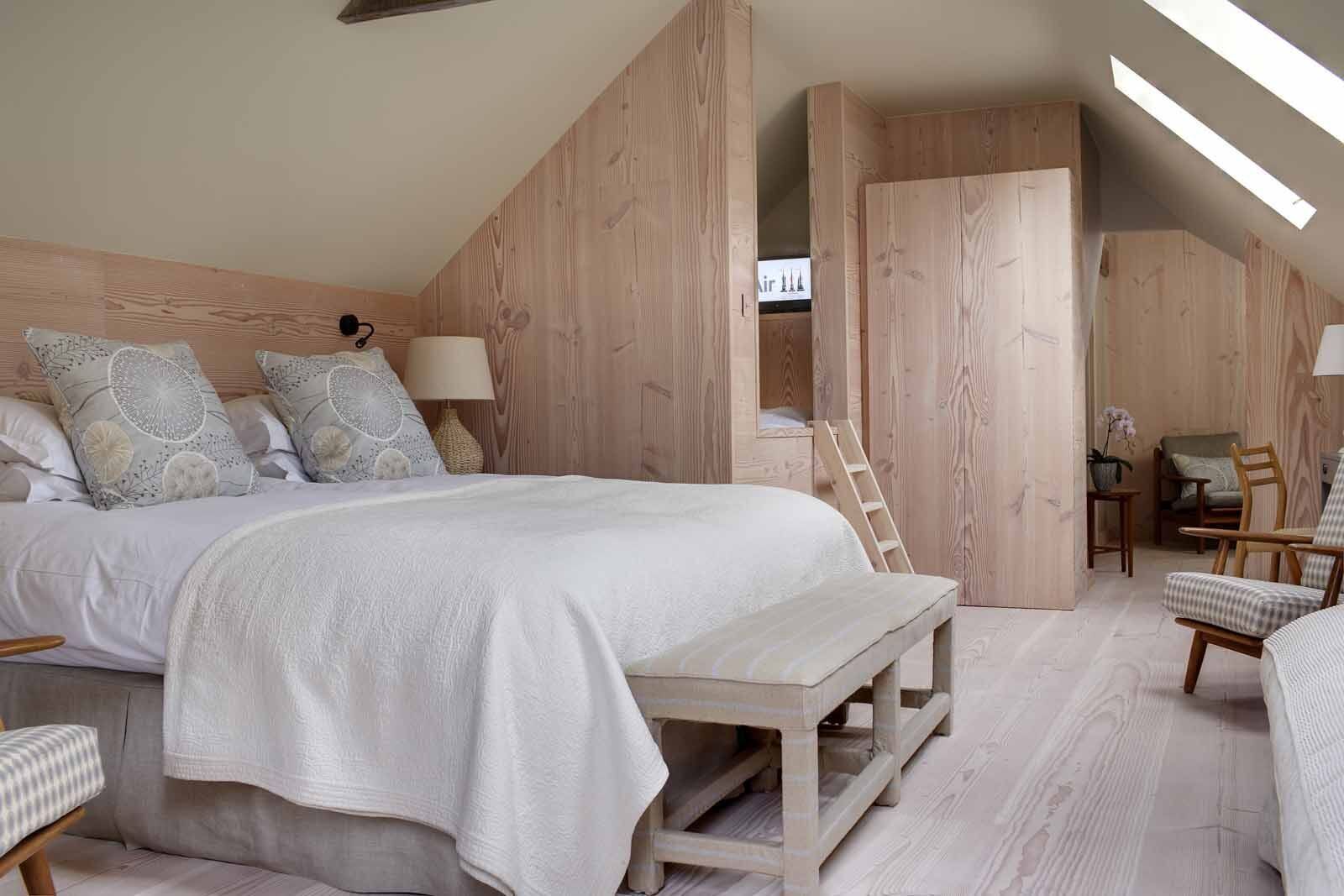 A bedroom with a large bed, wooden walls, a desk, and a chair.