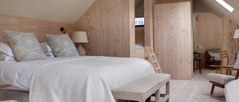 A bedroom with a large bed, wooden walls, a desk, and a chair.