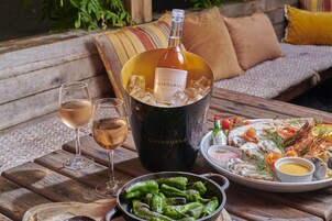 Una mesa con una botella de CUSBOURNE, dos copas de vino, un plato de mariscos y una bandeja de pimientos verdes.