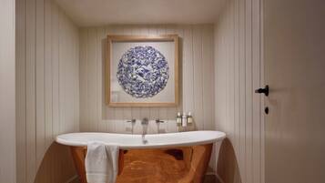 Une salle de bain avec une baignoire sur pieds, un meuble-lavabo en bois et un lavabo fixé au mur.