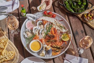 Una bandeja de mariscos con diversos elementos como ostras, camarones y pescado, acompañada de pan y una botella de salsa.