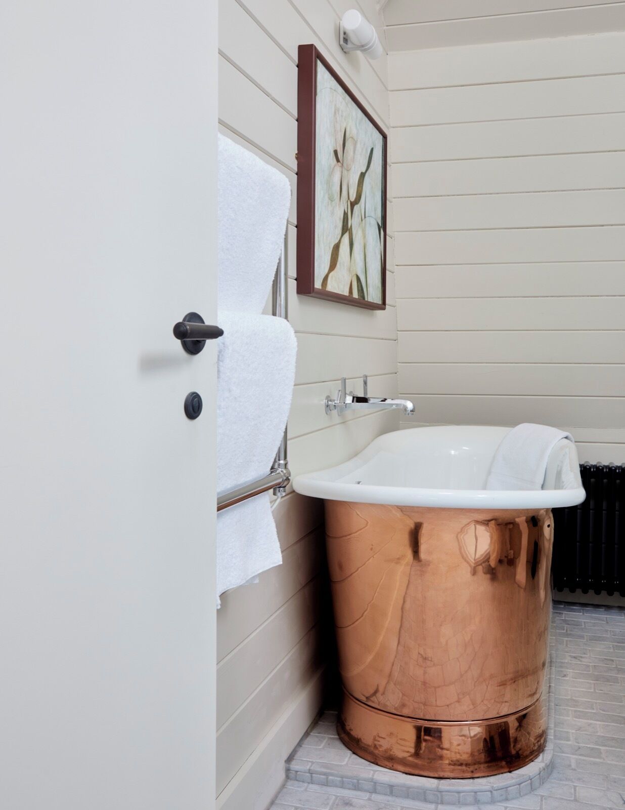 Un baño con una bañera de cobre, un lavamanos blanco y un perchero para toallas.