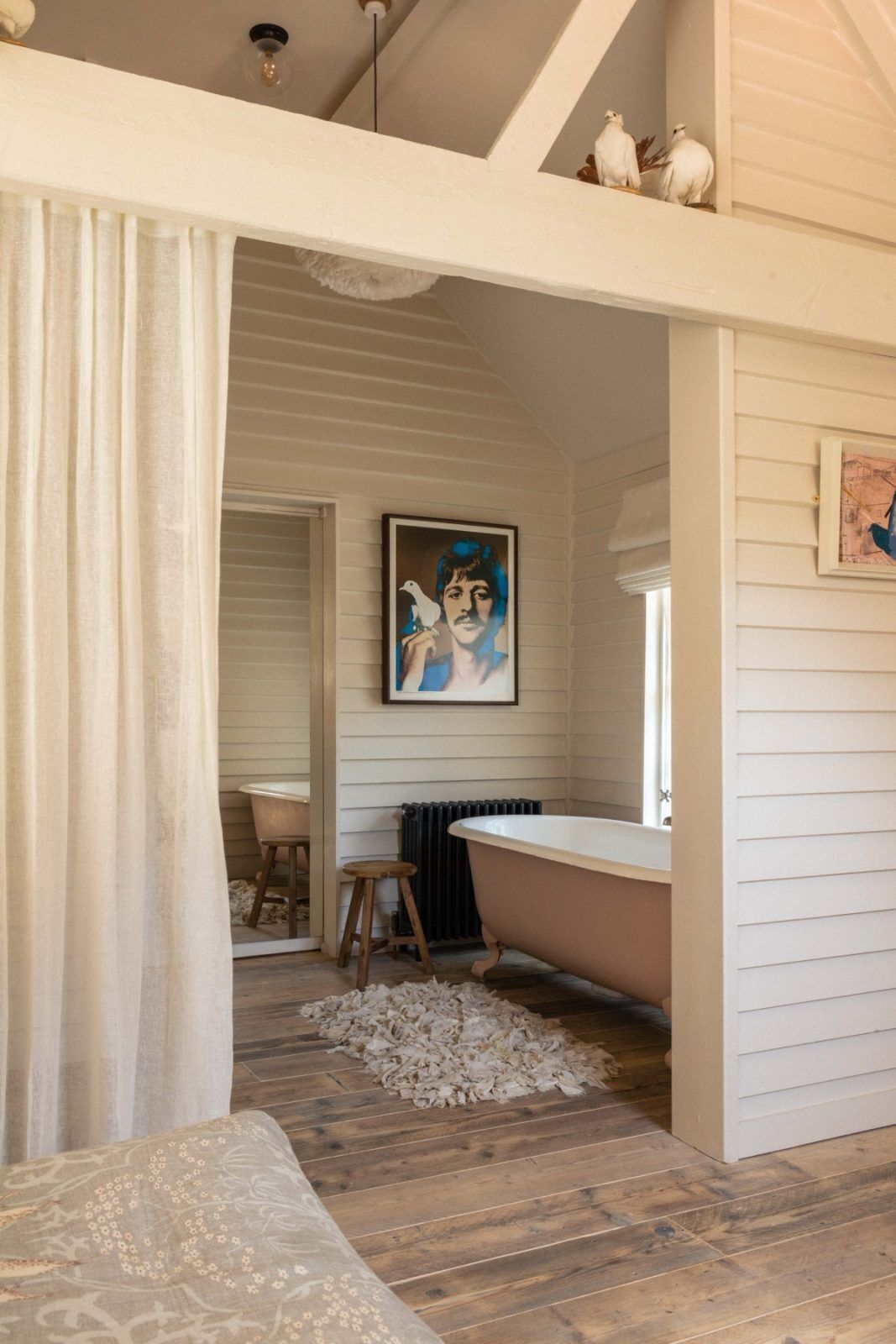 A bathroom with a bathtub, wooden floor, and a painting on the wall.