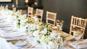 A long dining table set with white tablecloth, gold-rimmed glassware, and floral centerpieces.
