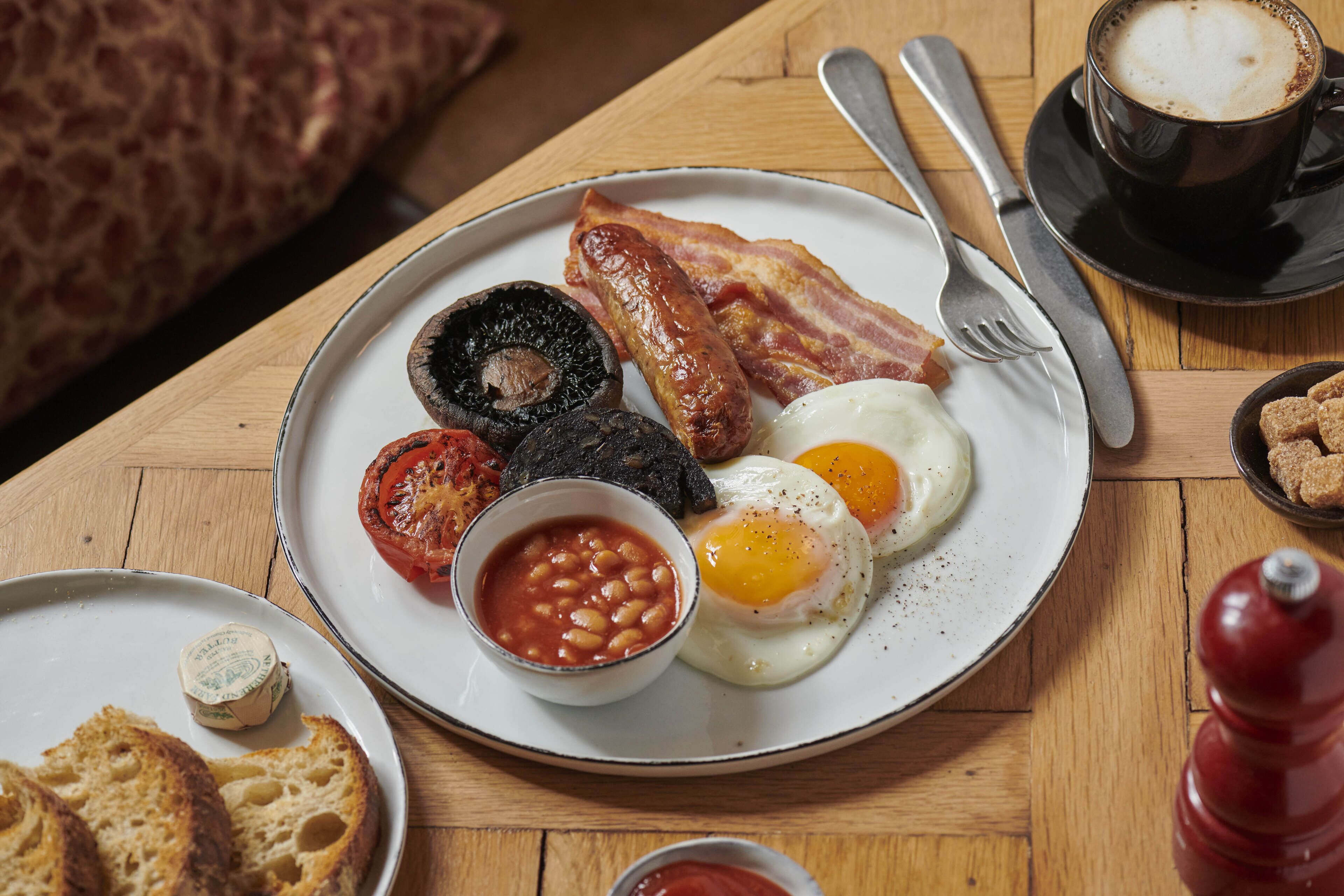 A breakfast plate with eggs, bacon, sausages, mushrooms, and beans.