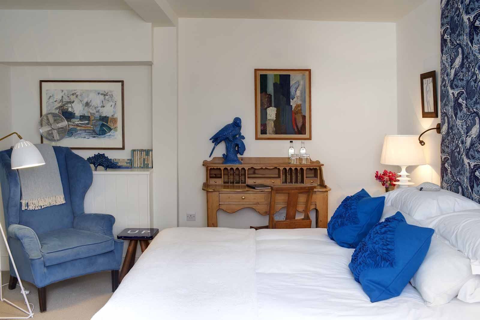 A hotel room with a bed, a desk, a chair, and artwork on the walls.