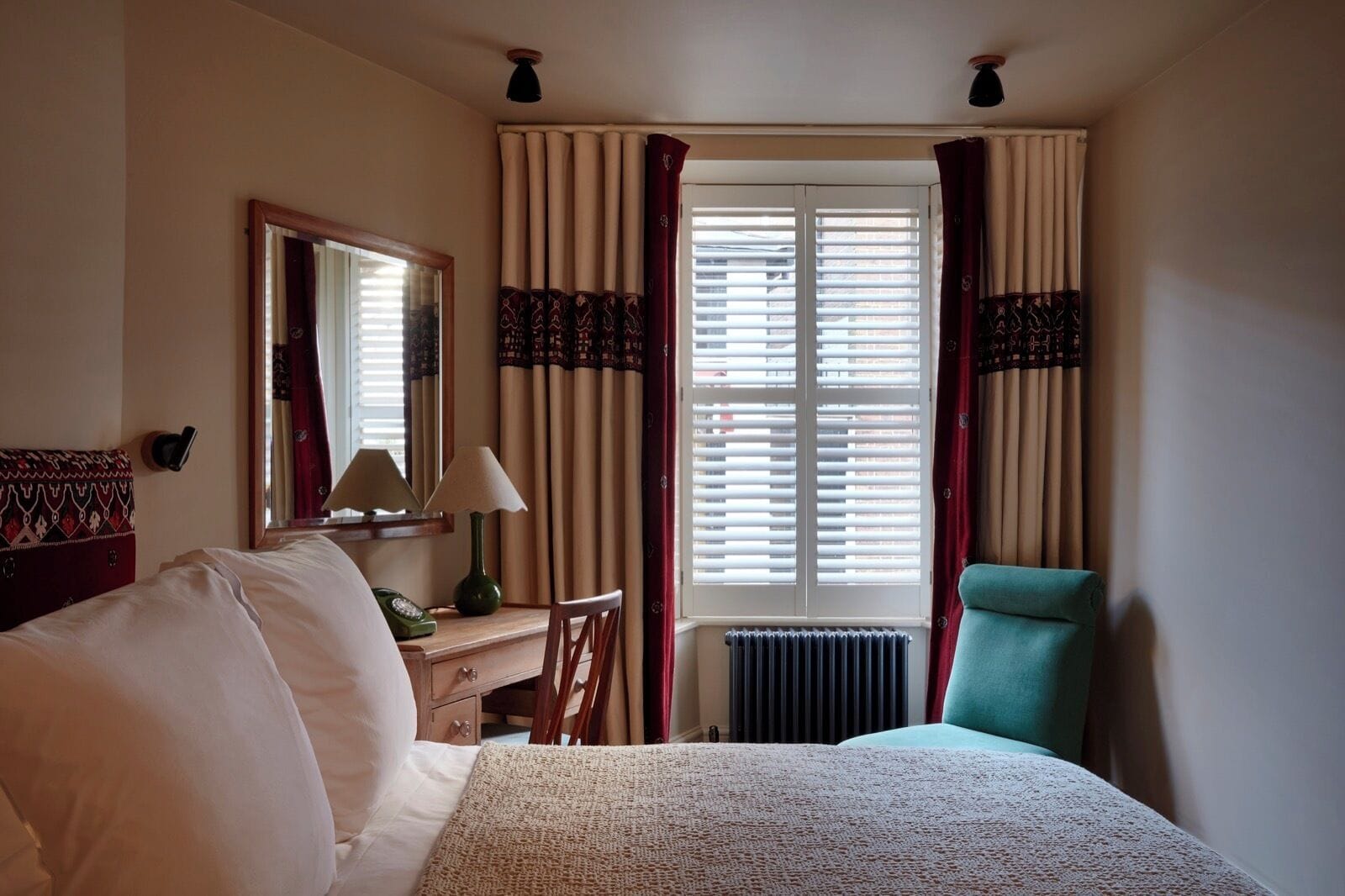 Ein Hotelzimmer mit einem Bett, einem Schreibtisch mit Lampe, einem Sessel und einem Fenster mit Vorhängen.