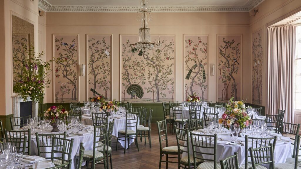 A formal dining room with multiple tables set for a meal, featuring green chairs and white tablecloths.