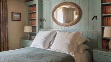 A bed with white linens, a round mirror on the wall, and a bookshelf with books.