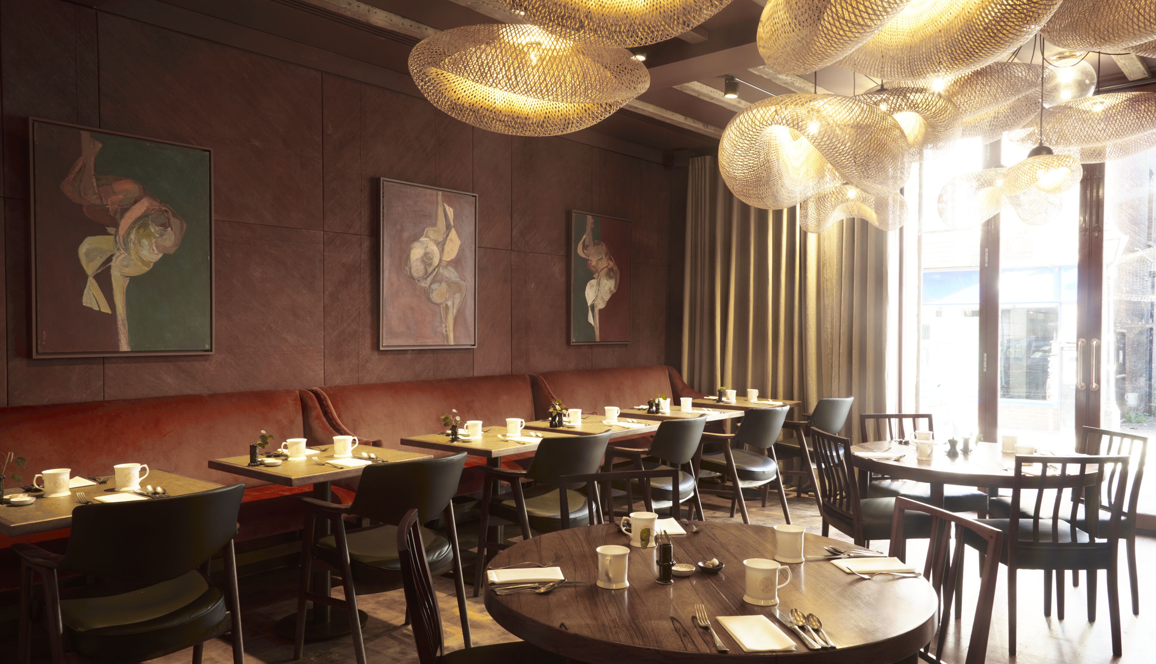 A restaurant with round tables, chairs, and hanging woven light fixtures.