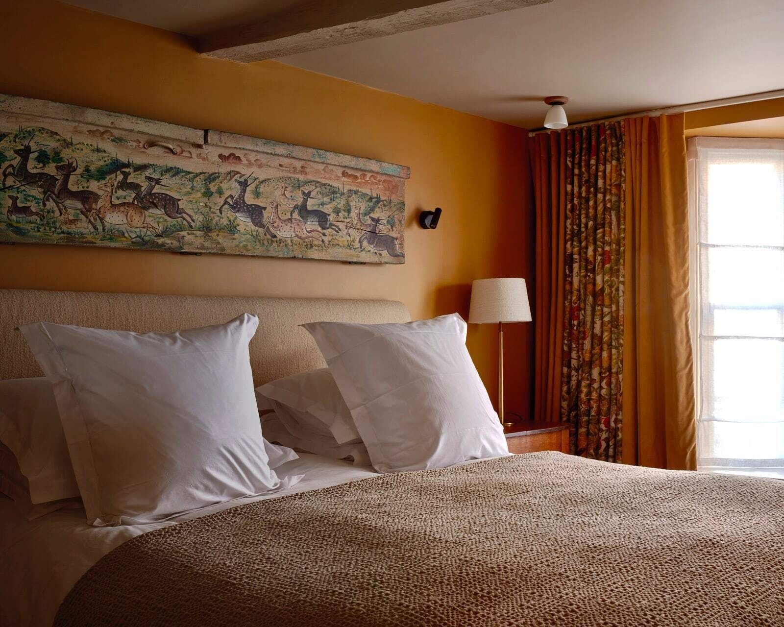 Habitación de hotel con una cama grande, un cuadro en la pared, una lámpara y una ventana con cortinas.