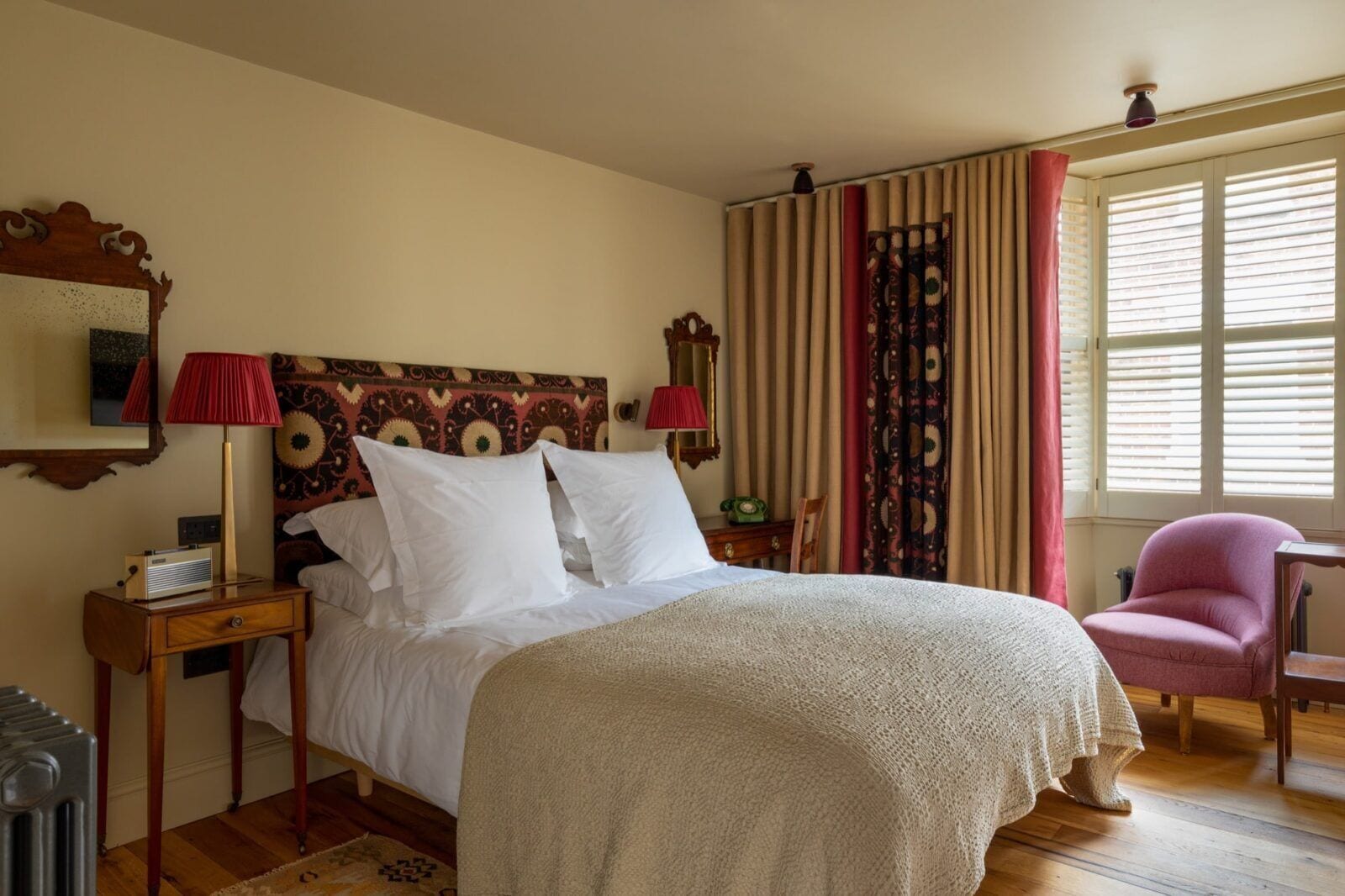 A neatly arranged bedroom with a bed, a bedside table with a lamp, a chair, and a window with curtains.