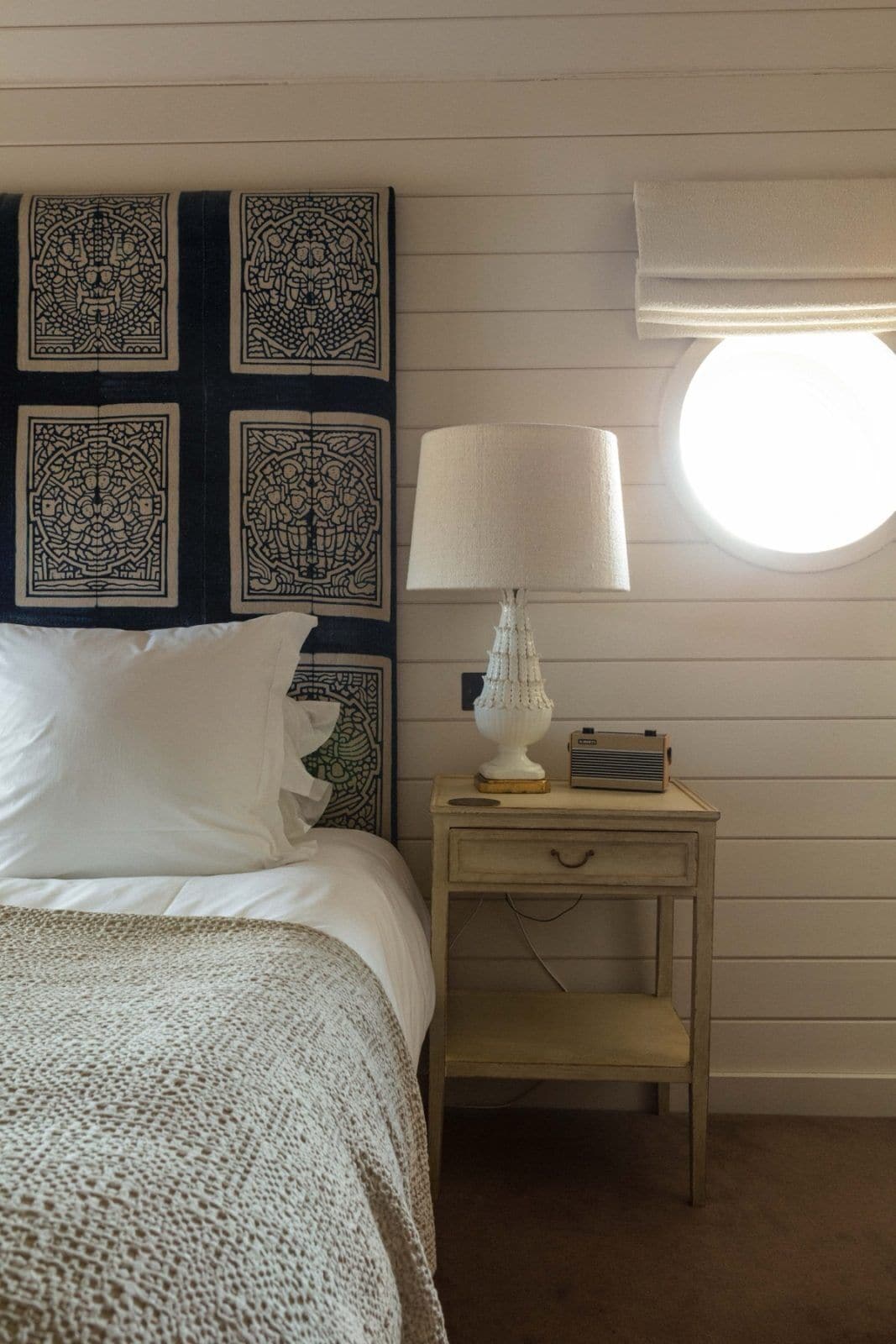 A bedroom with a bed, a nightstand with a lamp and radio, and decorative wall panels.