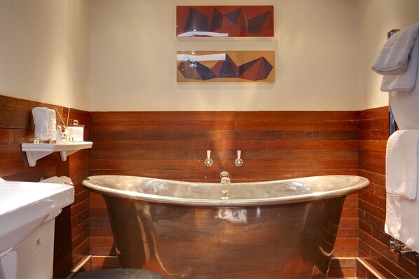 A bathroom with a freestanding bathtub, wooden paneling, a white sink, and two abstract paintings on the wall.