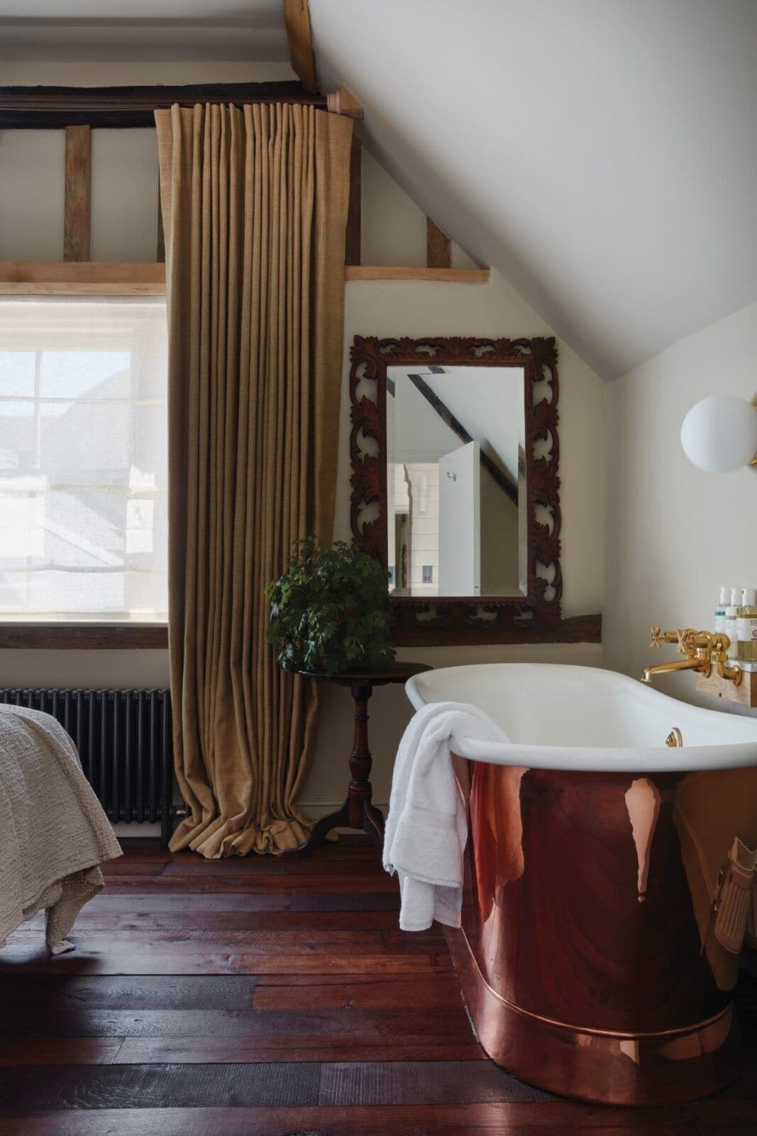 A bathroom with a wooden floor, a bathtub, a mirror, and a radiator.