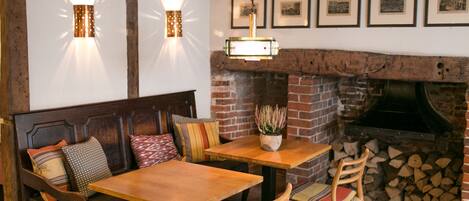 A cozy dining area with a wooden table and bench, a brick fireplace, and wall-mounted lights.