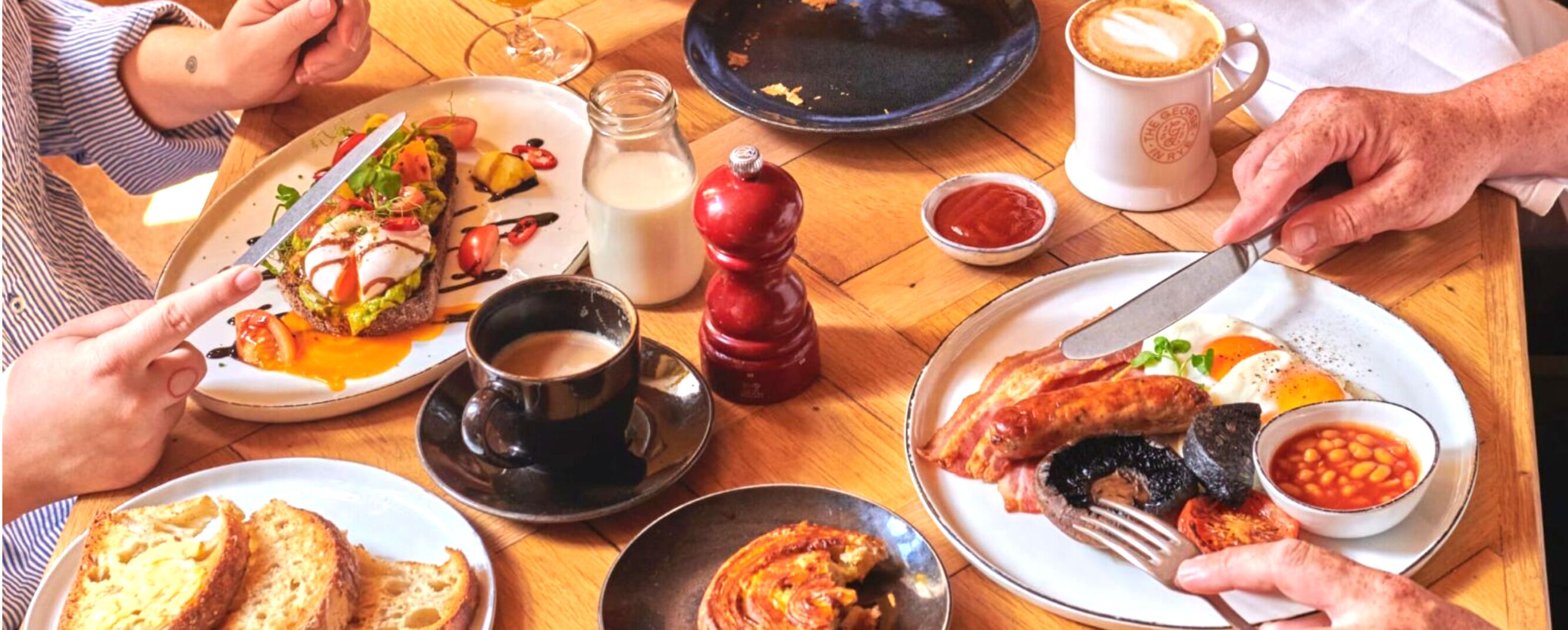 Una mesa de comedor con diversos platos, entre ellos tostadas, huevos, salchichas y frijoles.