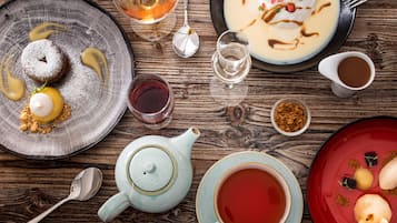 A wooden table with various dishes, including a dessert with powdered sugar, a bowl of soup with a dollop of cream, and a teapot with a cup of tea.