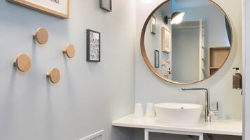 Un baño moderno con un espejo redondo, un lavamanos blanco y taburetes de madera.