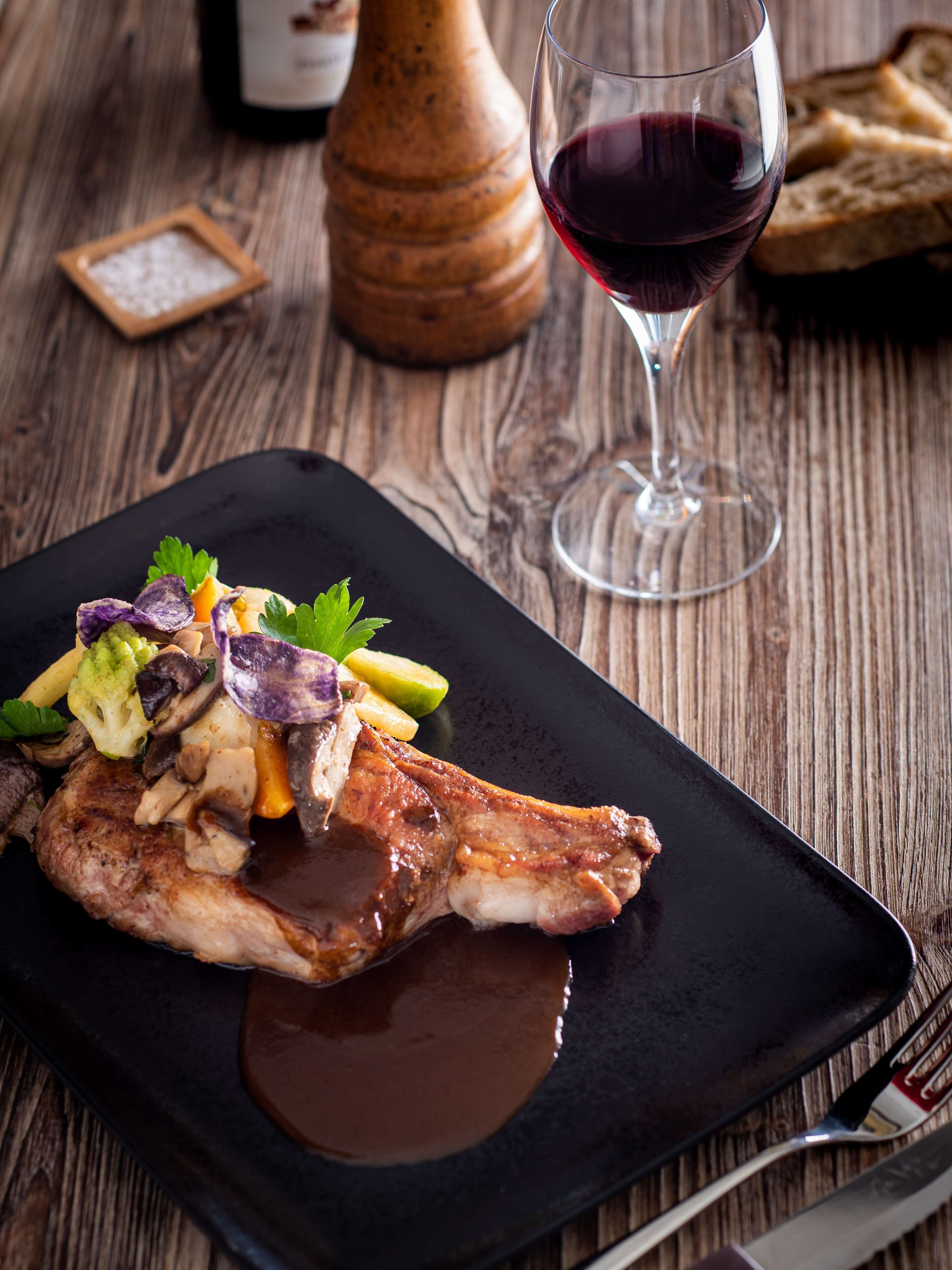 A plate of food with a glass of red wine and bread on a wooden table.