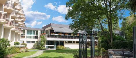 A modern building with a balcony overlooking a well-maintained garden.