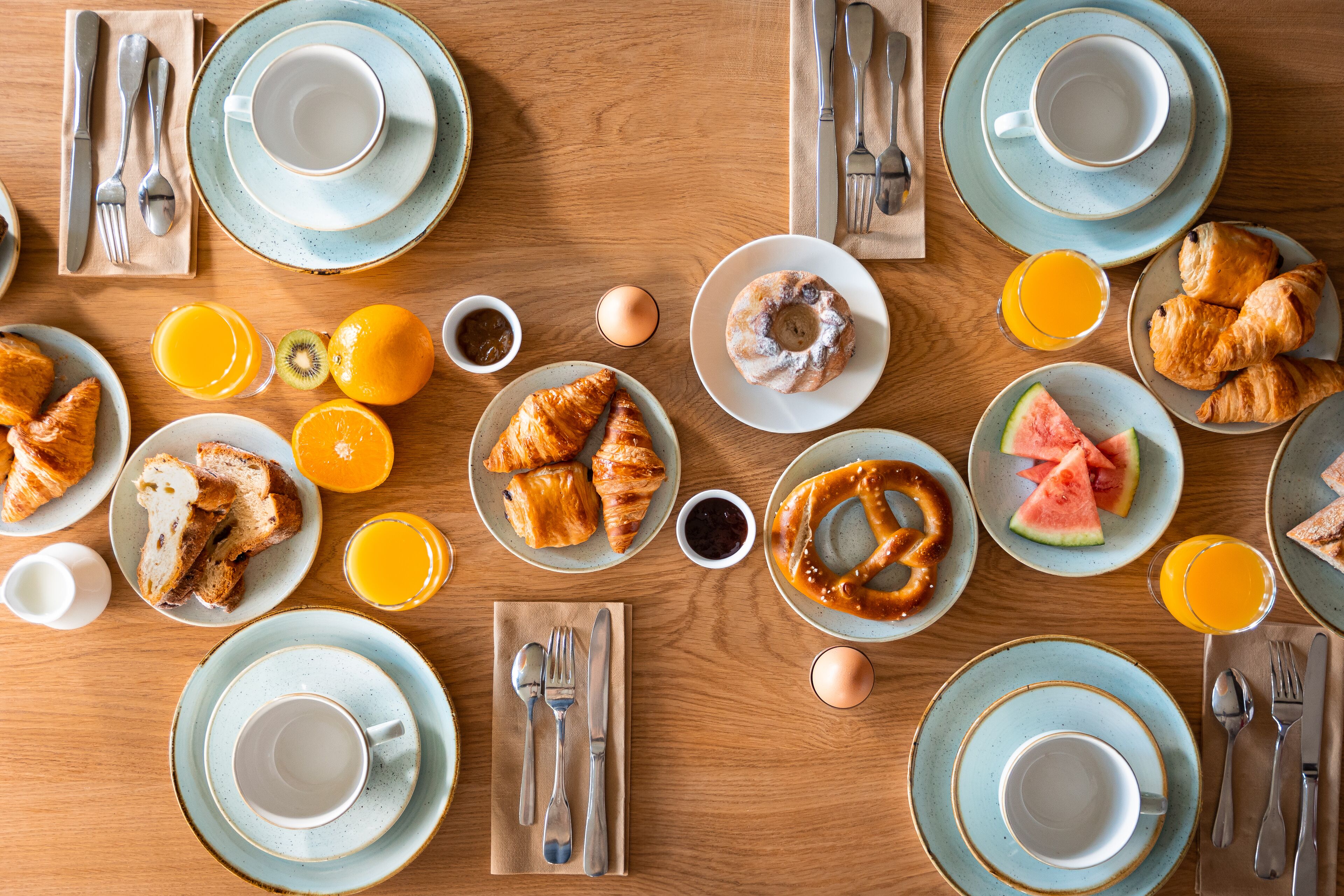 Een ontbijttafel met borden croissants, een bretzel en een croque-monsieur, plus sinaasappelsap en een glas sinaasappelsap.