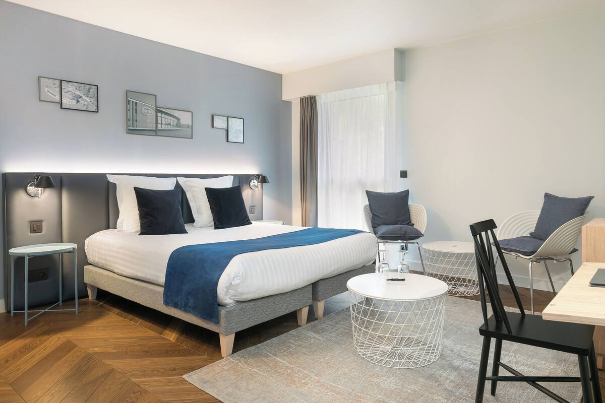A modern hotel room with a large bed, bedside tables, a desk, and chairs.