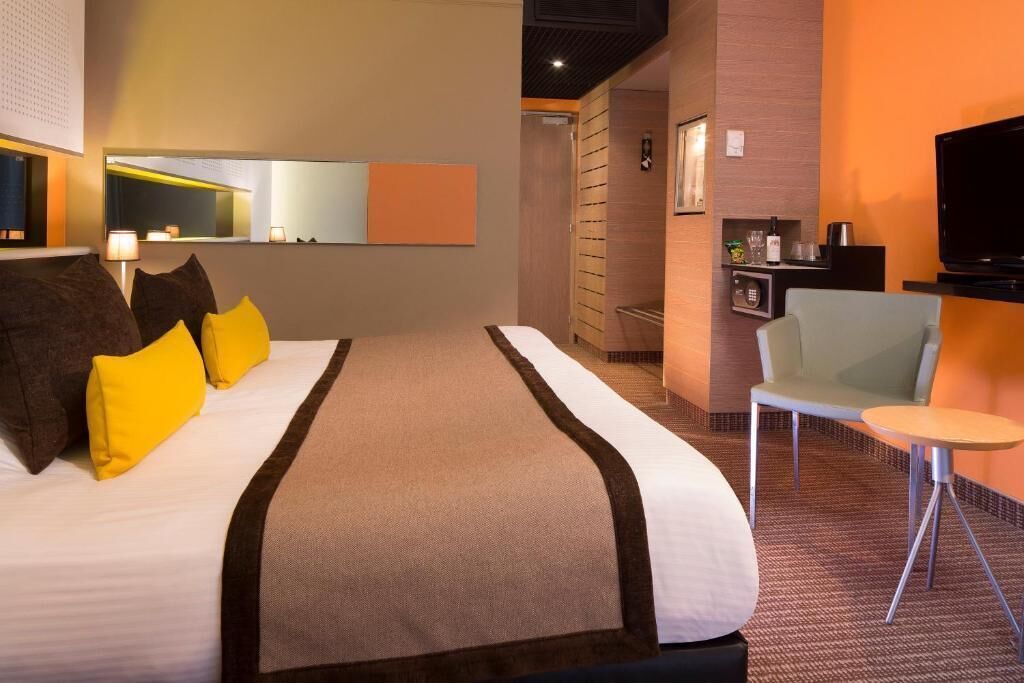 Habitación de hotel con una cama grande, un escritorio, una silla, un televisor y una mesita.