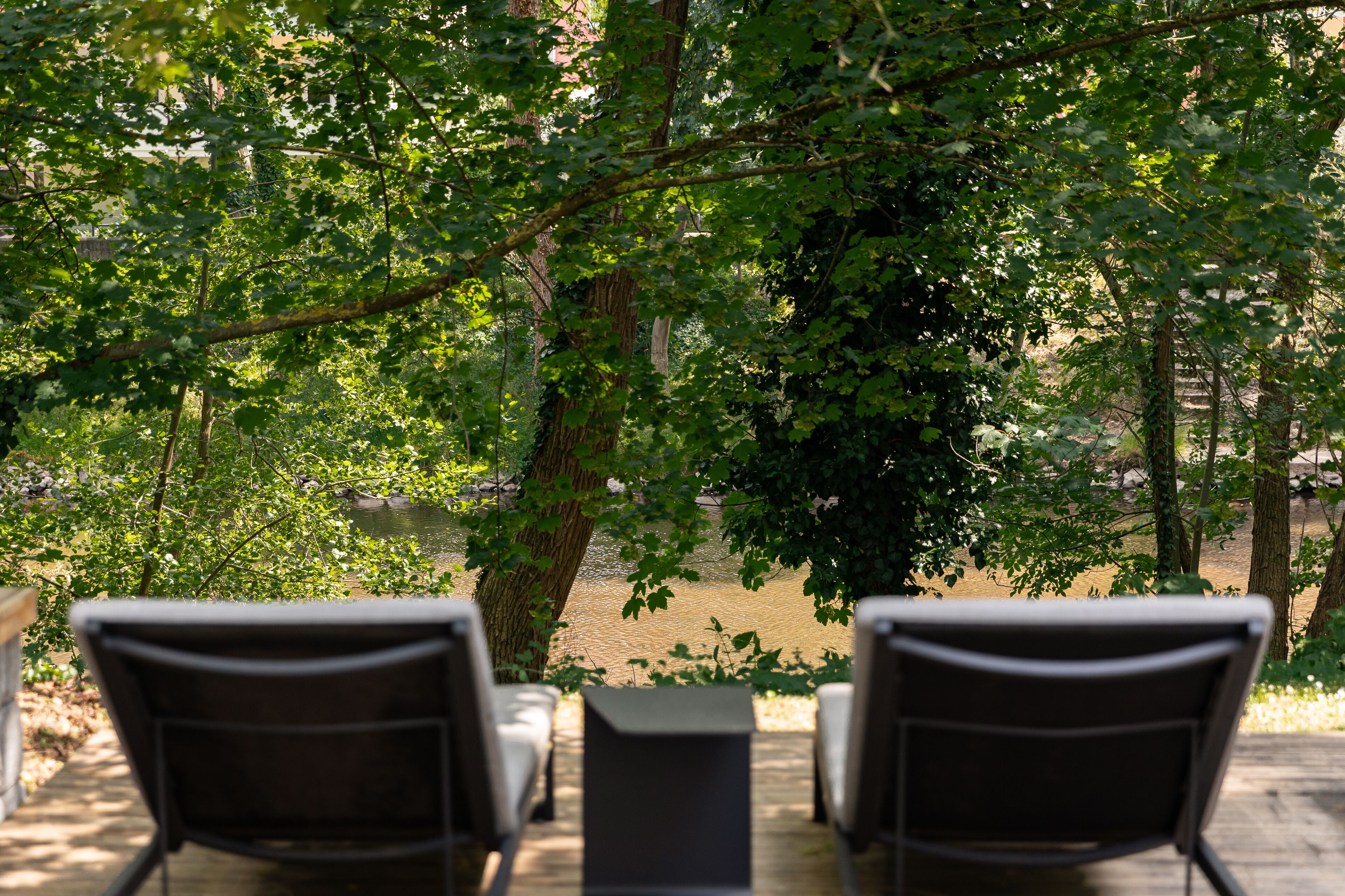 A deck with two chairs and a table, overlooking a river and surrounded by trees.