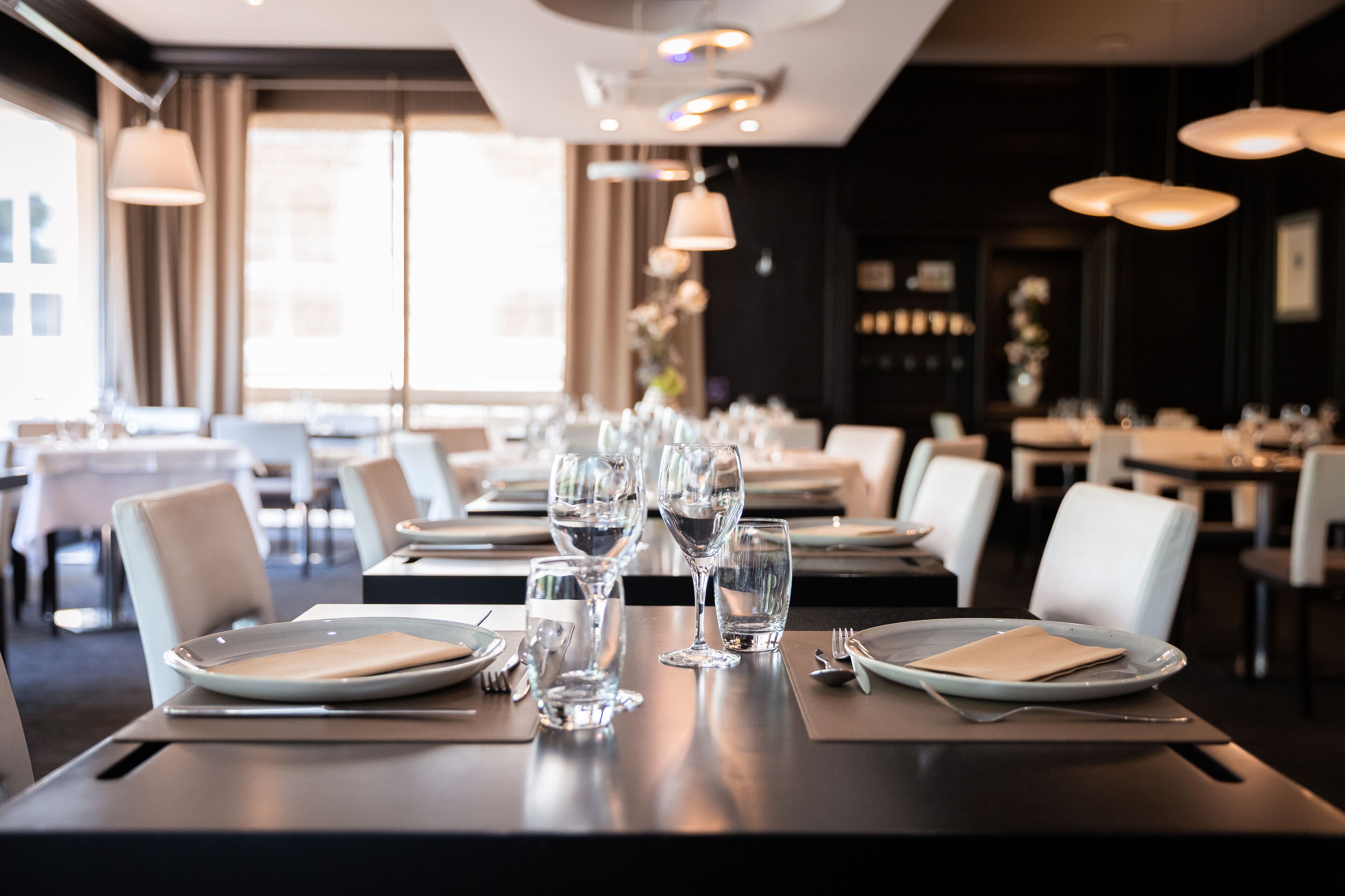 Un restaurante con mesas dispuestas para comer, destacando copas y platos de vidrio.