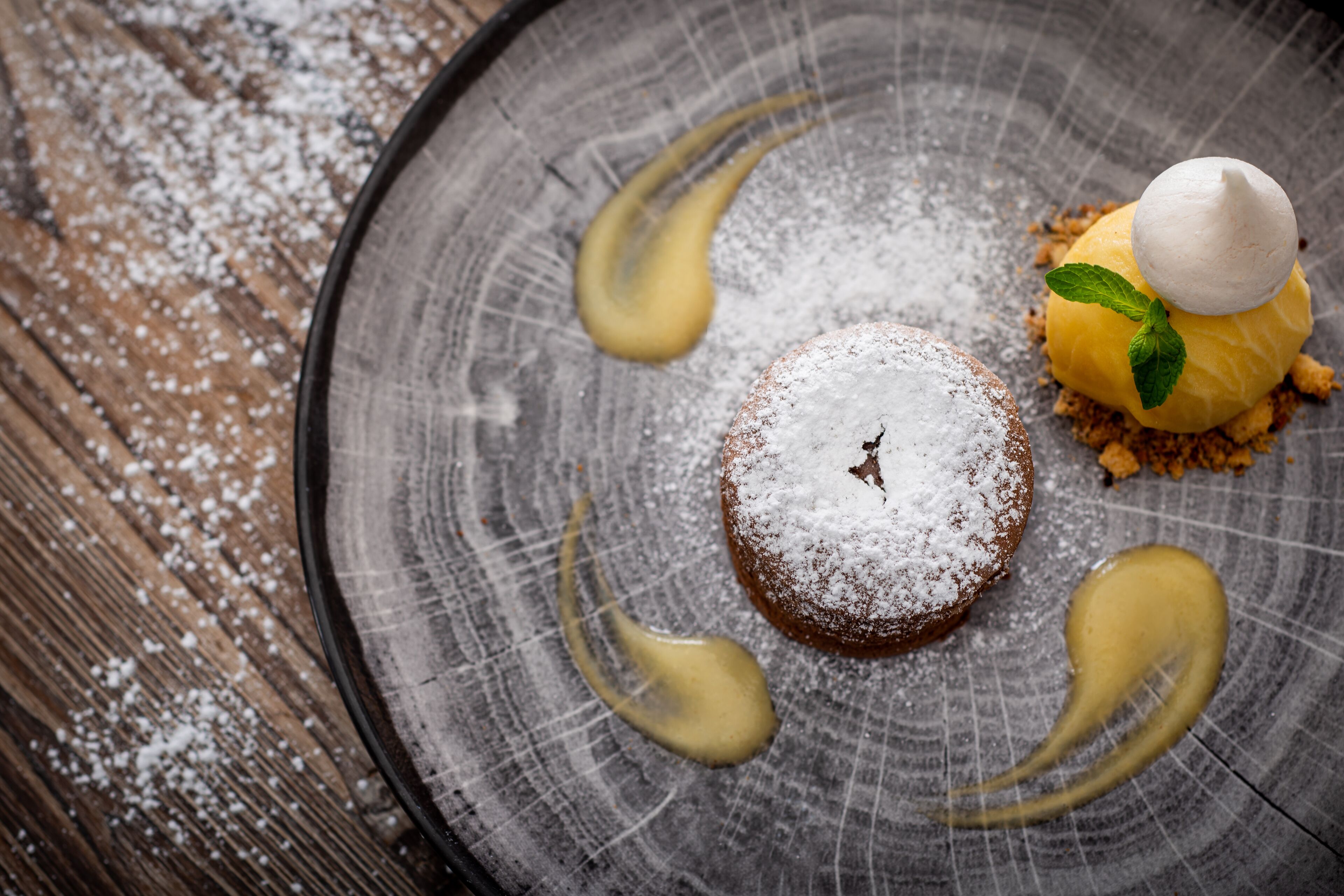 A dessert on a plate with powdered sugar and a mint leaf.