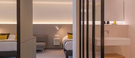 A modern hotel room with two beds, a small desk, and a built-in sink.
