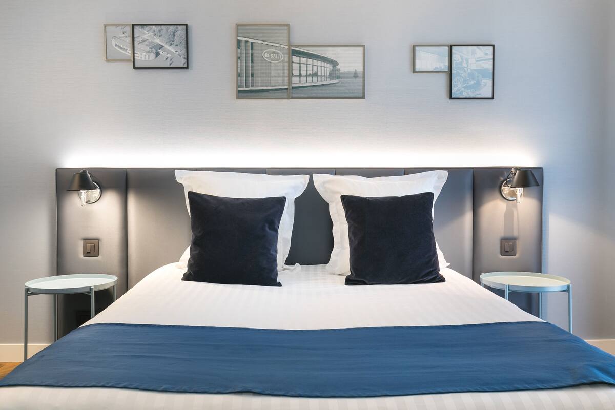 A modern hotel room with a large bed, two bedside tables, and wall-mounted artwork.