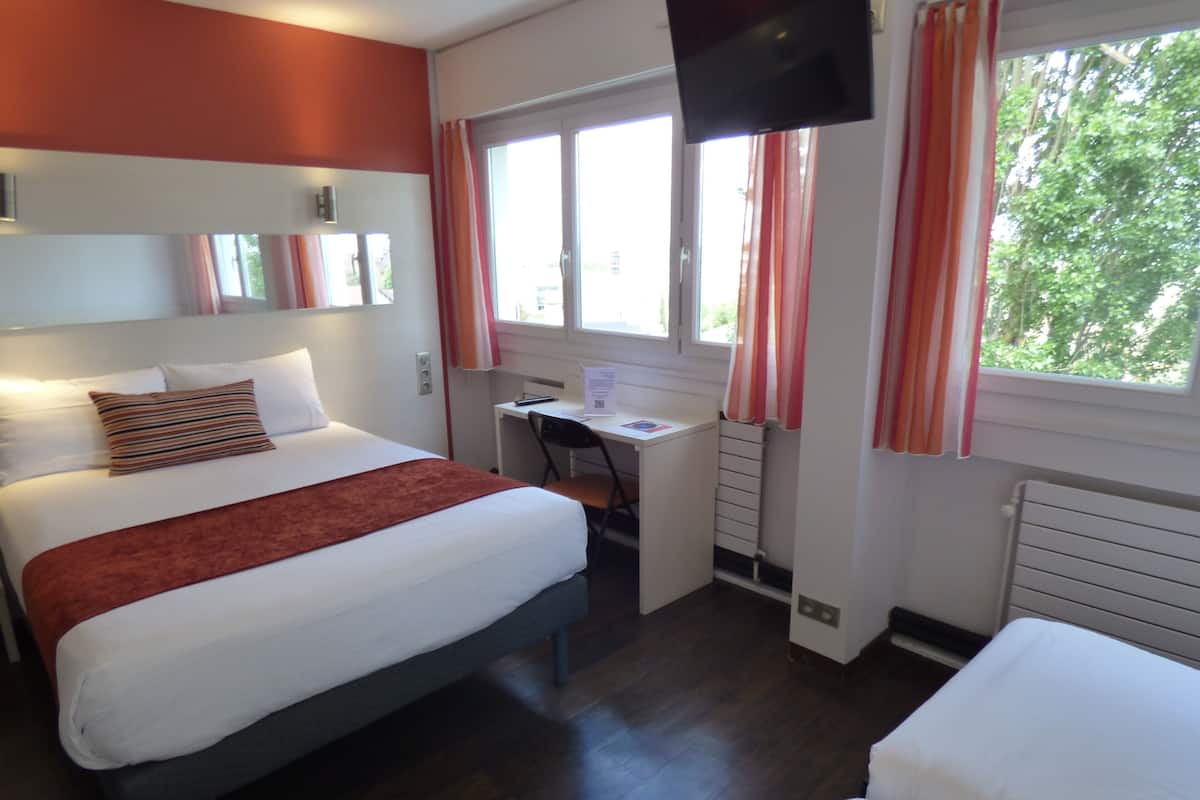 A hotel room with a bed, a desk, a TV, and a window with curtains.