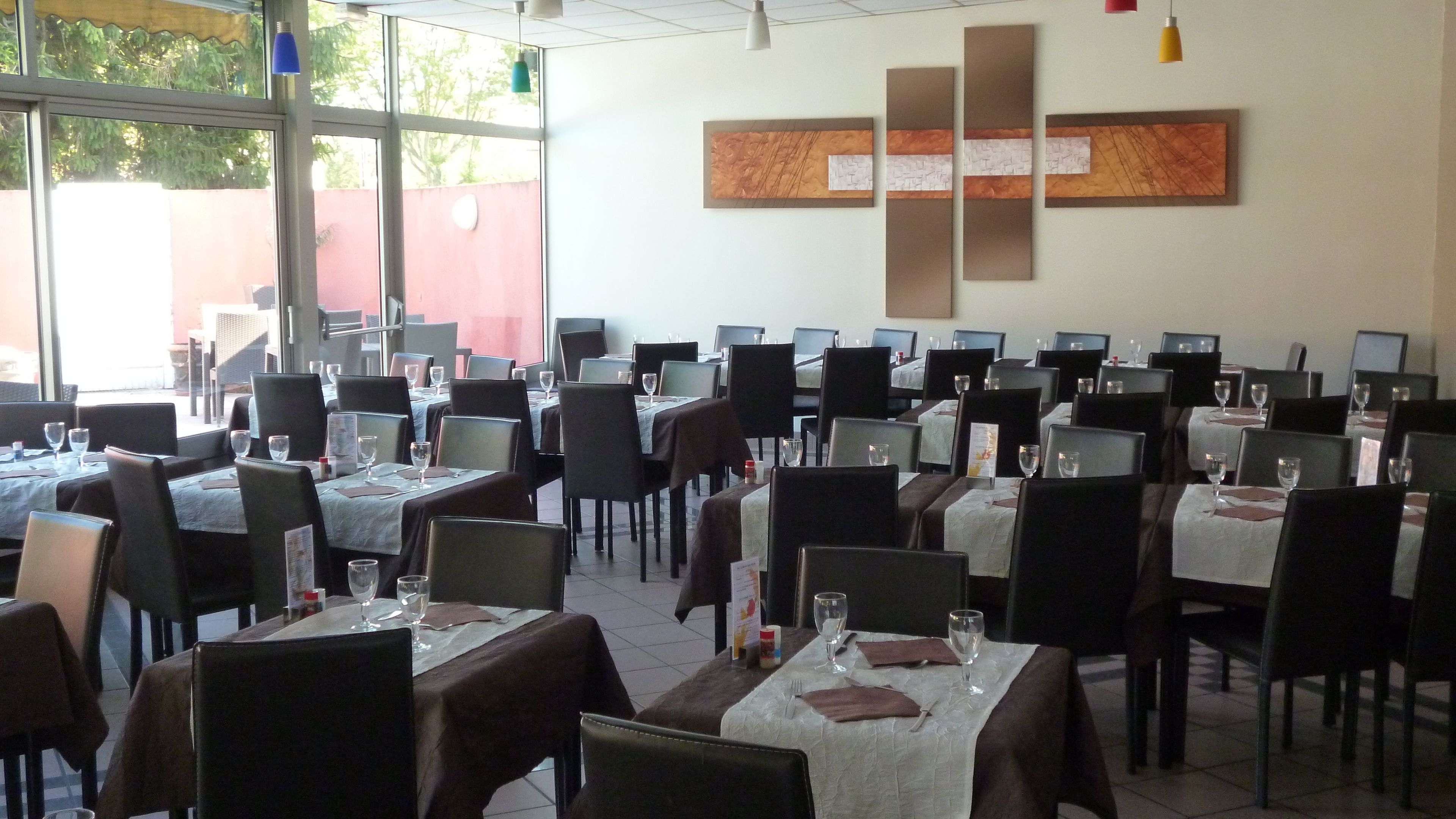 A dining area with tables set for service, chairs, and a large window with a view of trees.