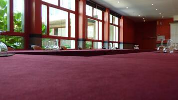 A conference room with a long table, chairs, and large windows with a view of greenery outside.