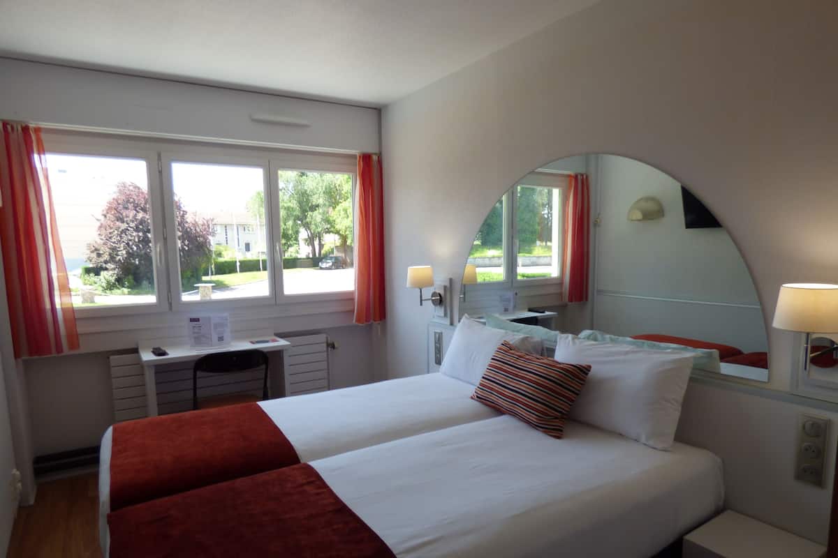 A hotel room with a bed, a desk, and a window with curtains.