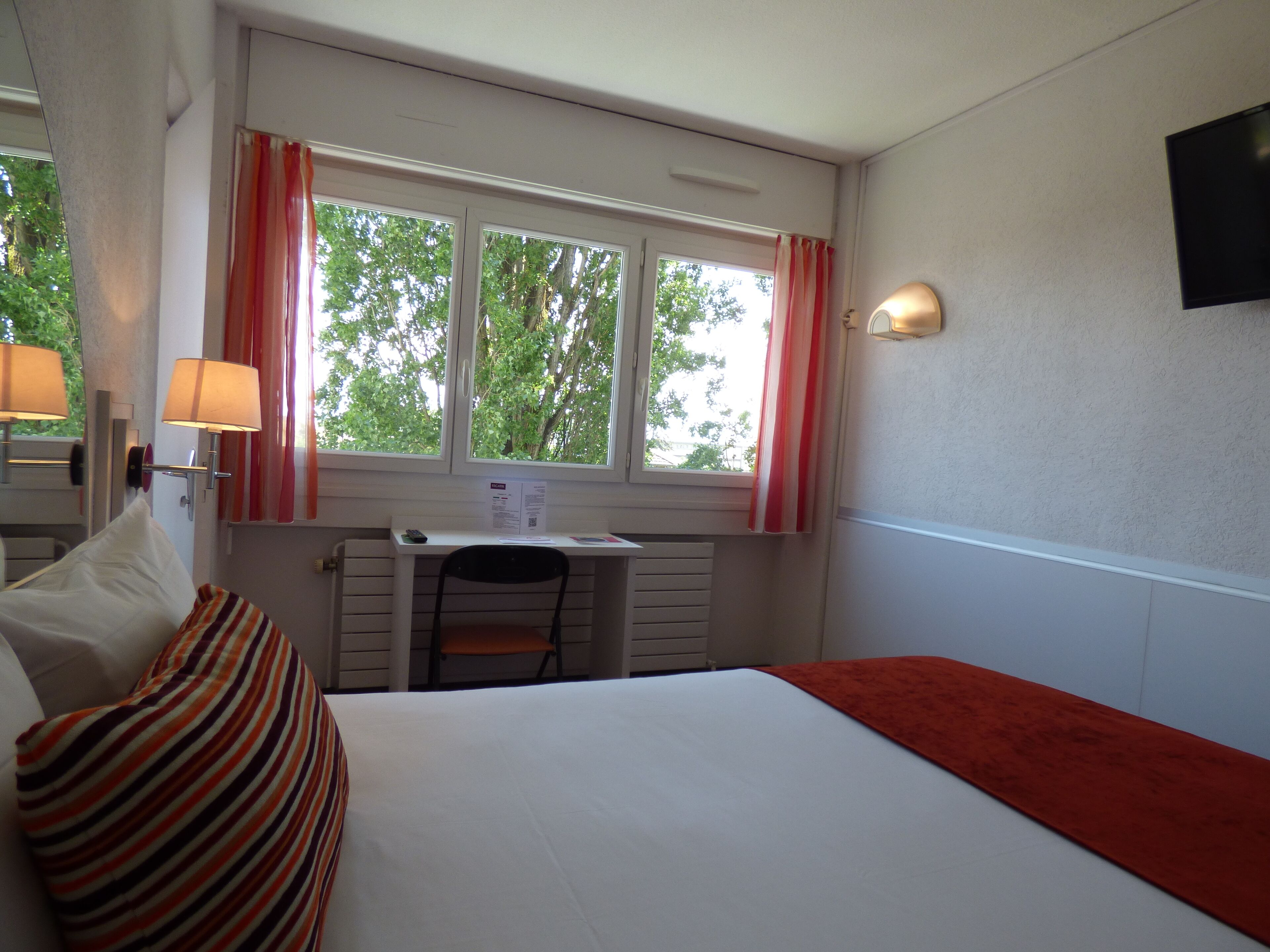 A hotel room with a bed, a desk, and a window with curtains.