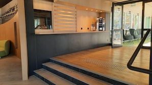 A modern reception area with a wooden reception desk, a coffee machine, and a seating area with chairs.