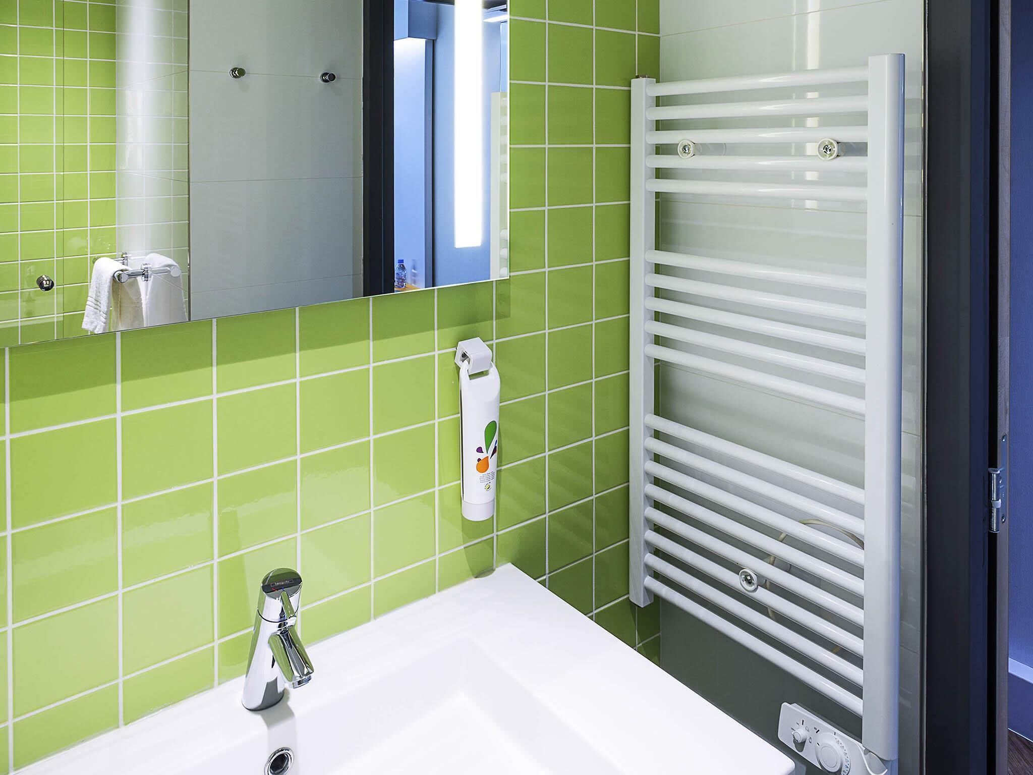 A bathroom with a white sink, green tiled walls, a mirror, and a white towel rack.