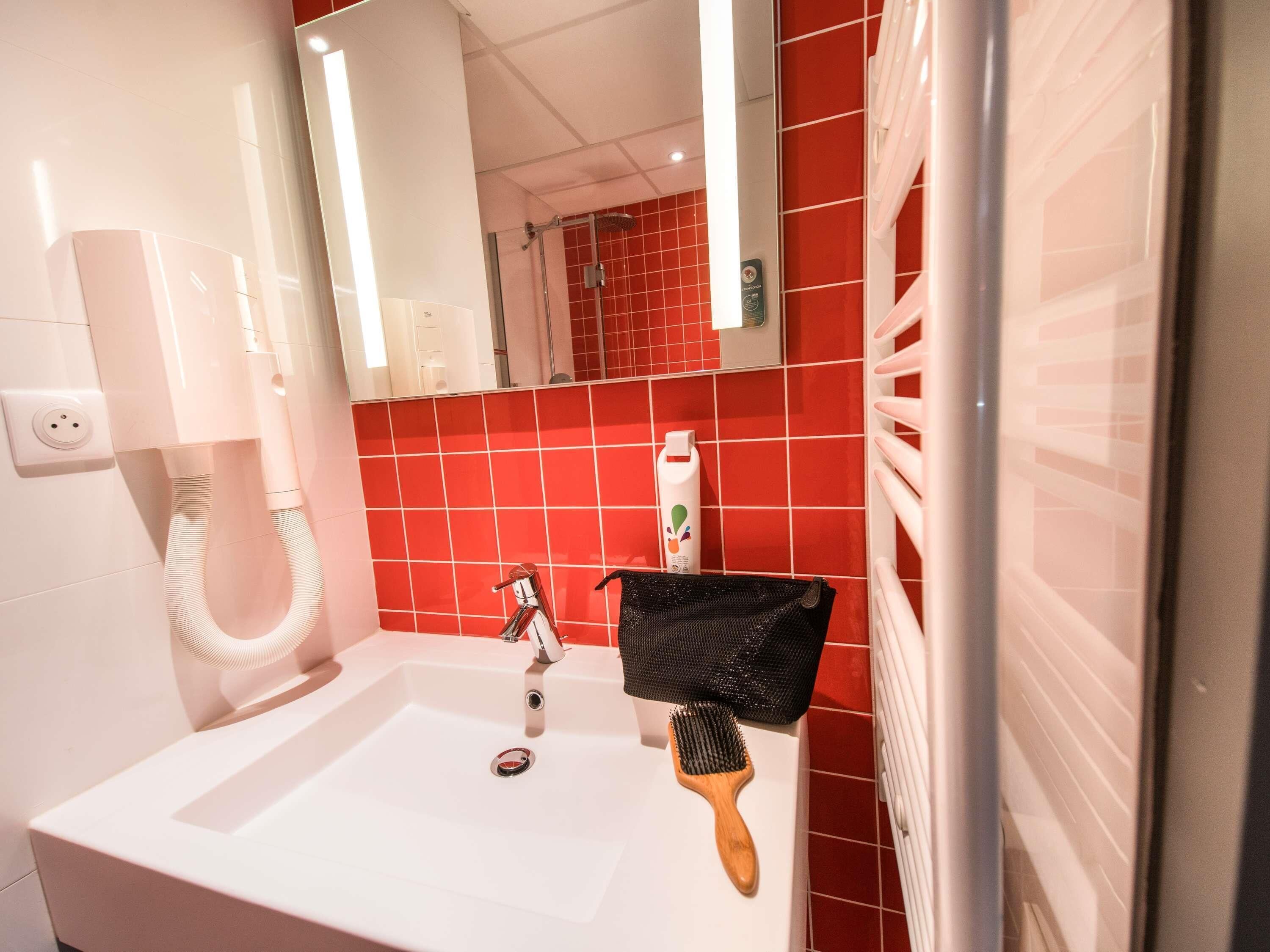 Een badkamer met een witte wastafel, rode betegelde wanden, een spiegel en een handdoekhouder.
