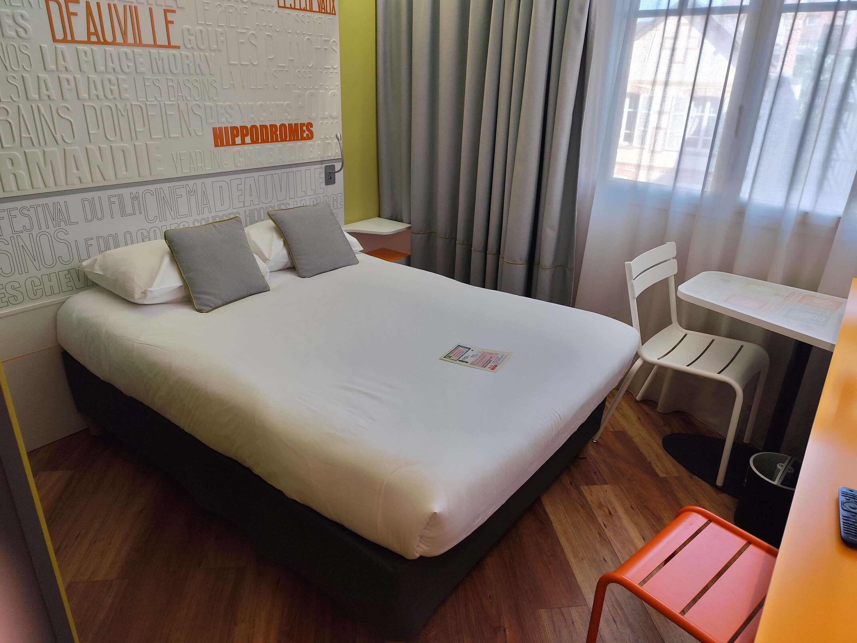 A hotel room with a bed, a desk, a chair, and a window with curtains.