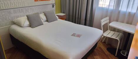 A hotel room with a bed, a desk, a chair, and a window with curtains.