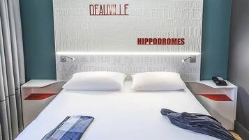 A modern hotel room with a white bed, a nightstand with a phone, and a wall with text.